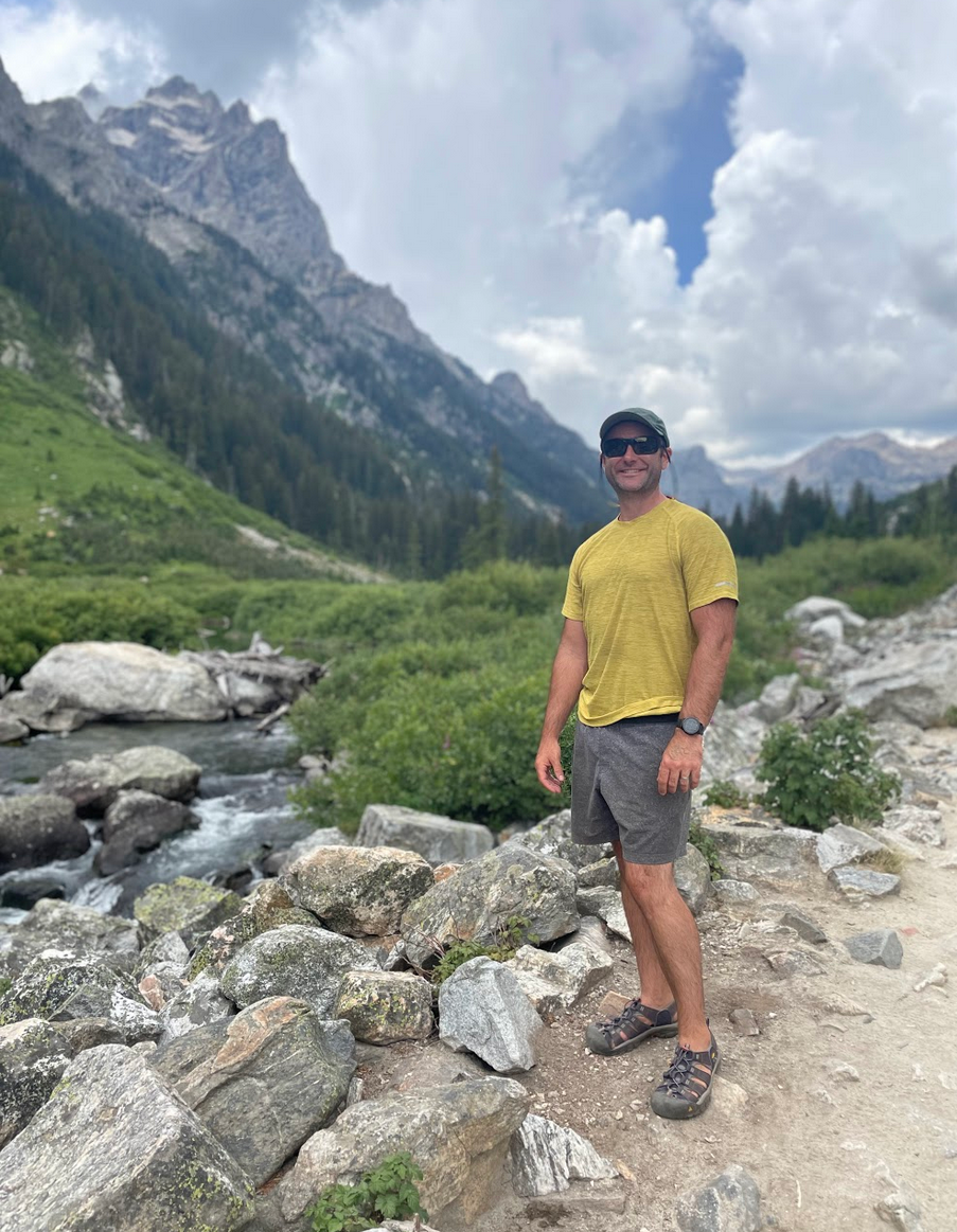 Professor Jesse Hampton standing in front of a mountain with green and rocky landscape.